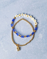 Set elastische kralen armband van Heinen Delfts Blauw. Eén armband heeft goudkleurige kraaltjes en een bedeltje van een tulp. De ander heeft goudkleurige kralen en kralen die het woord Amsterdam spellen. Set elastische kralen armband van Heinen Delfts Blauw. Eén armband heeft goudkleurige kraaltjes en een bedeltje van een tulp. De ander heeft goudkleurige kralen en kralen die het woord Amsterdam spellen.