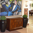Pair of black Bara Jar Tall Classic Vase Planters with topiary beside wood cabinet and large artwork