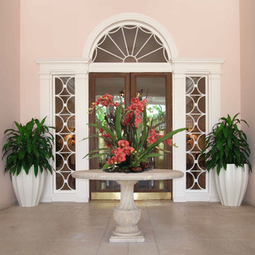 Alicante tapered fluted fiberglass planter pot in white finish with tall leafy plants beside entryway doors
