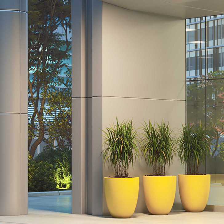 Valencia round fiberglass planter pots in yellow finish with tall green plants at modern building entrance