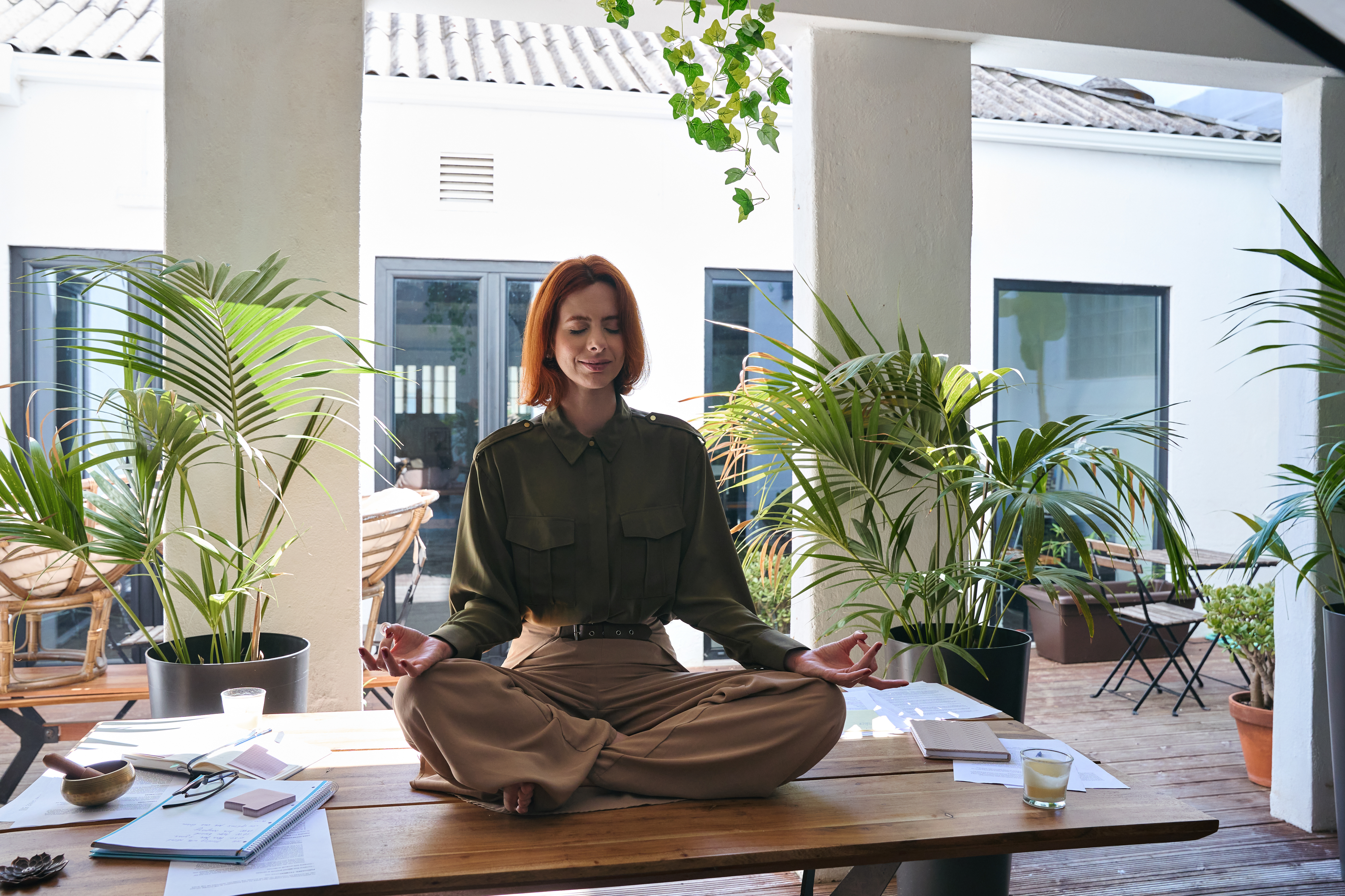 Employee sitting at a work desk and meditating around the office greenery