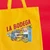 A mustard yellow canvas tote with the words "La Bodega" printed on it showing queso, plátanos, sazón, cafe, mangos, black beans, hot sauce, leche de coco, and more.