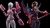Two action figures, one pink and white, the other red and black, on a reflective black surface with a dark background.