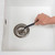 Hand using a sink unblocker tool in a white kitchen sink