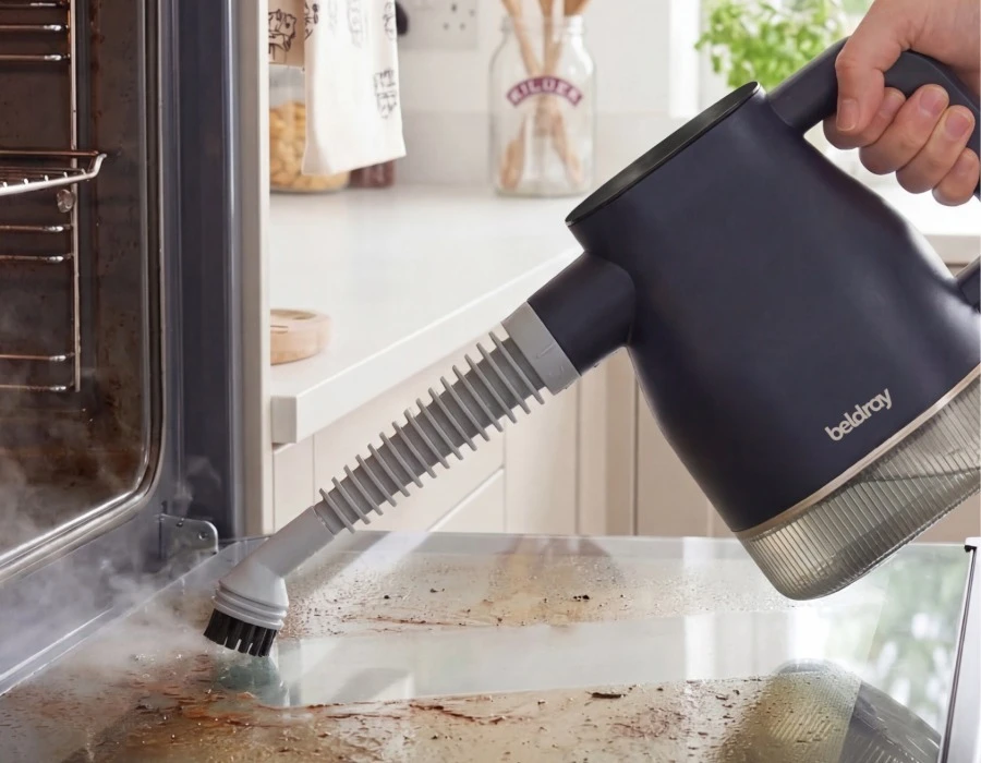 Digital Steam Cleaner with a brush attachment loosening grime from an oven door.