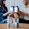 Two people exchange a gift box behind Neora's Advanced Skincare Set.