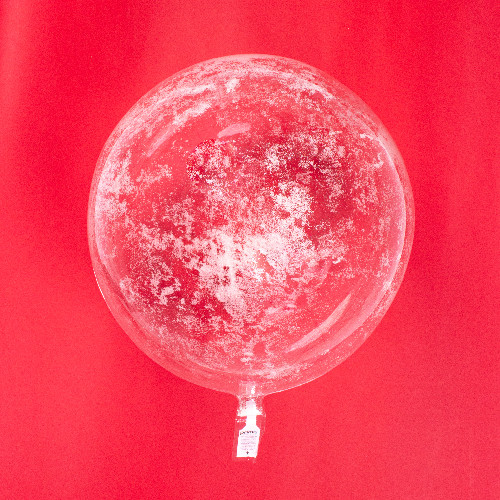 A 20 inch green, glow in the dark glitter clear sphere balloon in daylight