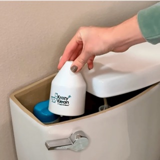 A hand placing a Krazy Klean capsule into a toilet tank