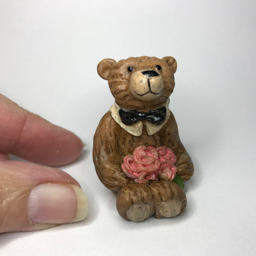 Seated itty bitty boy bear with a pink floral bouquet.