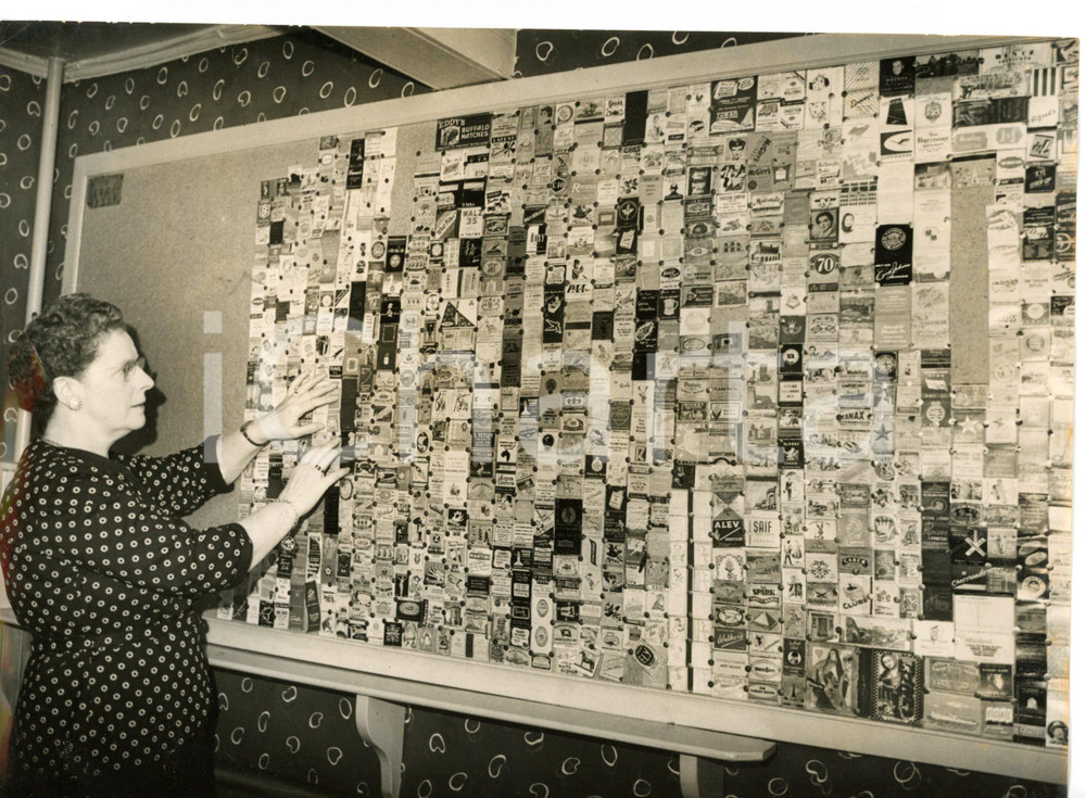 1957 PLYMOUTH Mrs. MOSEY fixing up match boxes on the wall of Allenby Arms *Foto Fotografia d'epoca con didascalia coeva. CONDIZIONI: FAIR (alone diffuso; piegatura al margine sinistro)DIMENSIONI: 20x15 cm     originale e autentica 1