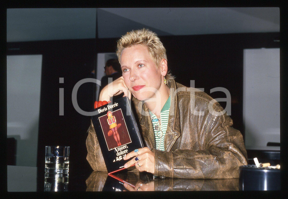 35mm vintage slide*1988 Doris DORRIE con il libro AMORE, DOLORE E TUTTO IL RESTO   Diapositiva d'epoca, in formato 35 mm. CONDIZIONI: GOODE' severamente vietata la riproduzione. Tutti i diritti sono riservati. ICharta mette in vendita, sul negozio eBay e in esclusiva sul sito "icharta" il proprio archivio composto da numerose diapositive e negativi fotografici d'epoca, tutti originali e autentici, che attraversano la storia del costume italiano tra gli la fine degli anni Sessanta e Novanta.Si tratta di uno sguardo inedito sull'attualit&agrave;, la politica, la vita quotidiana, il gossip e la cultura, che fotografa il cambiamento della nazione in quest'ultimo scorcio del XX secolo. Un'occasione unica per il mercato del collezionismo, che vede finalmente disponibile un archivio eccezionale per vastit&agrave;, tematiche e condizioni, in un settore (il negativo fotografico e la diapositiva) di assoluta novit&agrave; e dalle interessanti prospettive di investimento.  originale e autentica 1