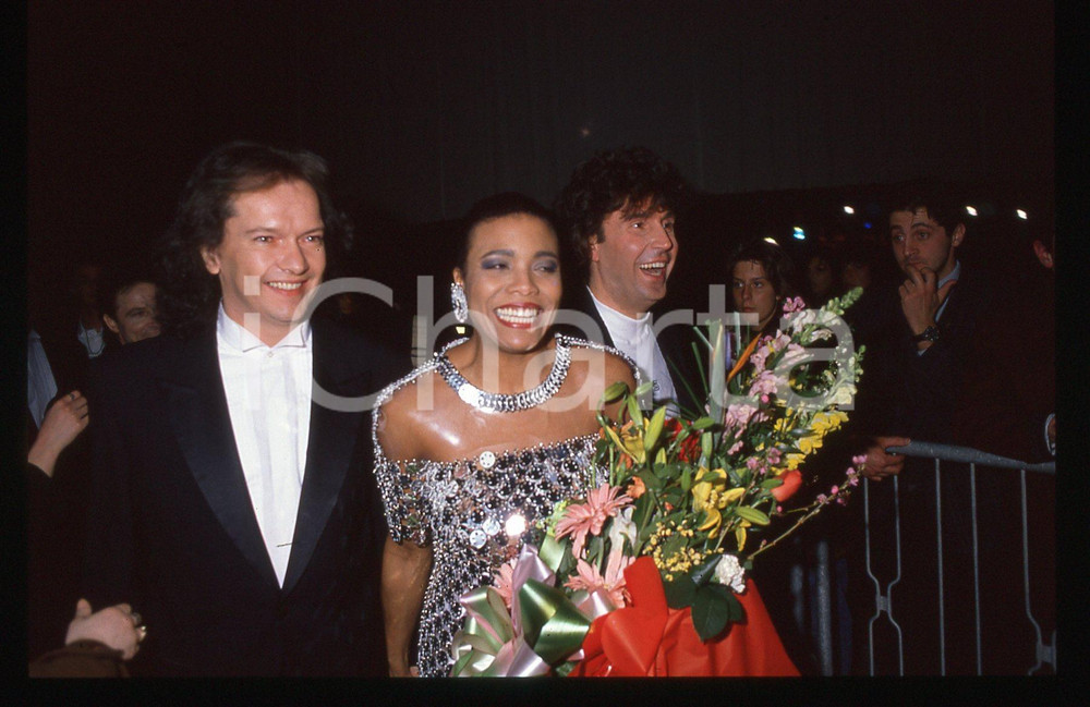 35mm vintage slide* 1990 Festival SANREMO - Didi BRIDGEWATER e Stefano D'ORAZIO   Diapositiva d'epoca, in formato 35 mm.Nella diapositiva Didi BRIDGEWATER, Stefano D'ORAZIO e Red CANZIAN dei Pooh al Festival di Sanremo del 1990. CONDIZIONI: GOODE' severamente vietata la riproduzione. Tutti i diritti sono riservati. ICharta mette in vendita, sul negozio eBay e in esclusiva sul sito "icharta" il proprio archivio composto da numerose diapositive e negativi fotografici d'epoca, tutti originali e autentici, che attraversano la storia del costume italiano tra gli la fine degli anni Sessanta e Novanta.Si tratta di uno sguardo inedito sull'attualit&agrave;, la politica, la vita quotidiana, il gossip e la cultura, che fotografa il cambiamento della nazione in quest'ultimo scorcio del XX secolo. Un'occasione unica per il mercato del collezionismo, che vede finalmente disponibile un archivio eccezionale per vastit&agrave;, tematiche e condizioni, in un settore (il negativo fotografico e la diapositiva) di assoluta novit&agrave; e dalle interessanti prospettive di investimento.  originale e autentica 1