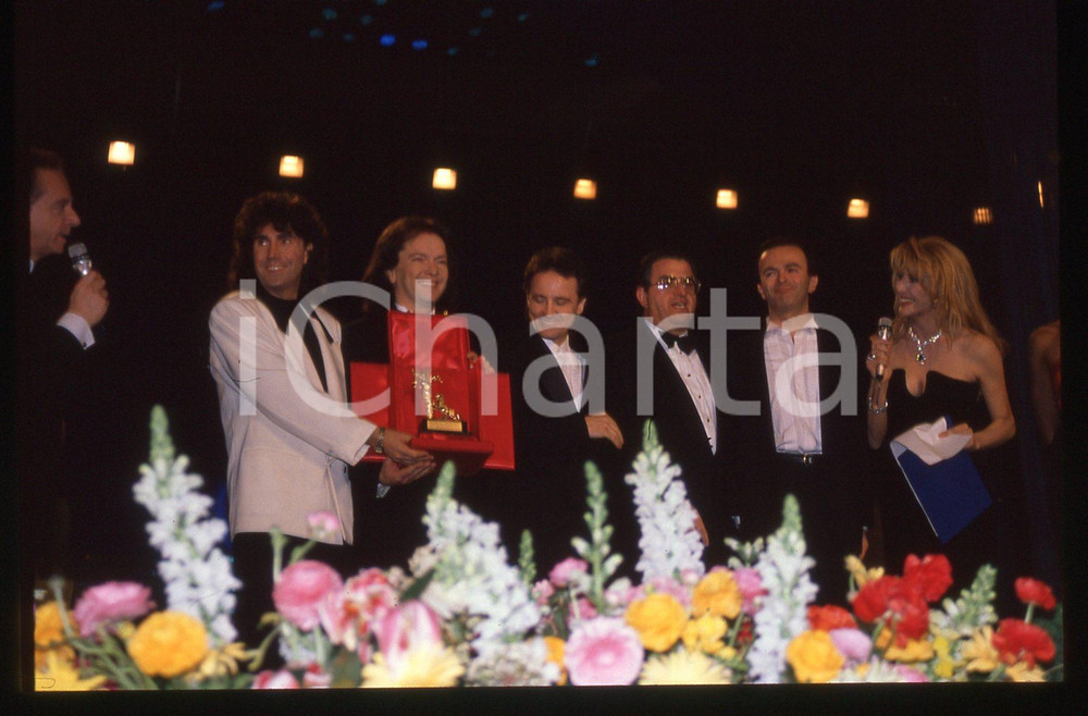 35mm vintage slide* 1990 Festival SANREMO Johnny DORELLI POOH Gabriella CARLUCCI   Diapositiva d'epoca, in formato 35 mm.Nella diapositiva i componenti del gruppo musicale POOH (Roby Facchinetti, Dodi Battaglia, Stefano D'Orazio e Red Canzian) con Gabriella Carlucci e Johnny Dorelli sul palcoscenico del Festival di Sanremo del 1990. CONDIZIONI: GOODE' severamente vietata la riproduzione. Tutti i diritti sono riservati. ICharta mette in vendita, sul negozio eBay e in esclusiva sul sito "icharta" il proprio archivio composto da numerose diapositive e negativi fotografici d'epoca, tutti originali e autentici, che attraversano la storia del costume italiano tra gli la fine degli anni Sessanta e Novanta.Si tratta di uno sguardo inedito sull'attualit&agrave;, la politica, la vita quotidiana, il gossip e la cultura, che fotografa il cambiamento della nazione in quest'ultimo scorcio del XX secolo. Un'occasione unica per il mercato del collezionismo, che vede finalmente disponibile un archivio eccezionale per vastit&agrave;, tematiche e condizioni, in un settore (il negativo fotografico e la diapositiva) di assoluta novit&agrave; e dalle interessanti prospettive di investimento.  originale e autentica 1