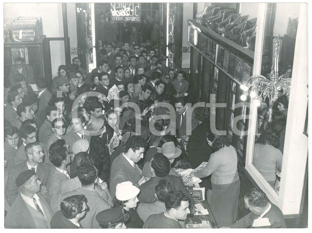 1957 NAPOLI Tenore Mario DEL MONACO al negozio CURCI tra i fan - Foto Fotografia d'epoca, con didascalia dattiloscritta coeva al verso. POOR/danneggiato piegature angolari e lievi sovraimpressioni al lato superiore Formato: 24x18 cm originale e autentica 1