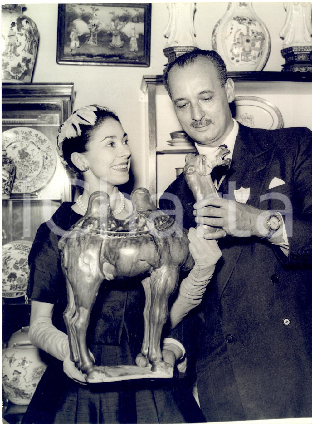 1958 LONDON Antique dealer George HAND shows a model camel to Margot FONTEYN