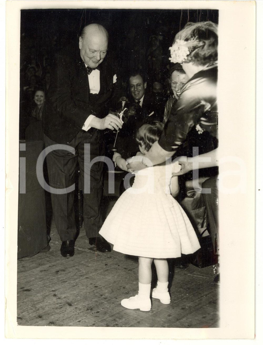 1954 LONDON Royal Albert Hall - Sir Winston CHURCHILL giving a flower to a baby Fotografia d'epoca, con didascalia coeva al verso.  CONDIZIONI: POOR (piegatura al margine inferiore; rigature al margine superiore; strappo millimetrico al margine sinistro; piccola sovraimpressione) CONDIZIONI: 15x20 cm    originale e autentica 1