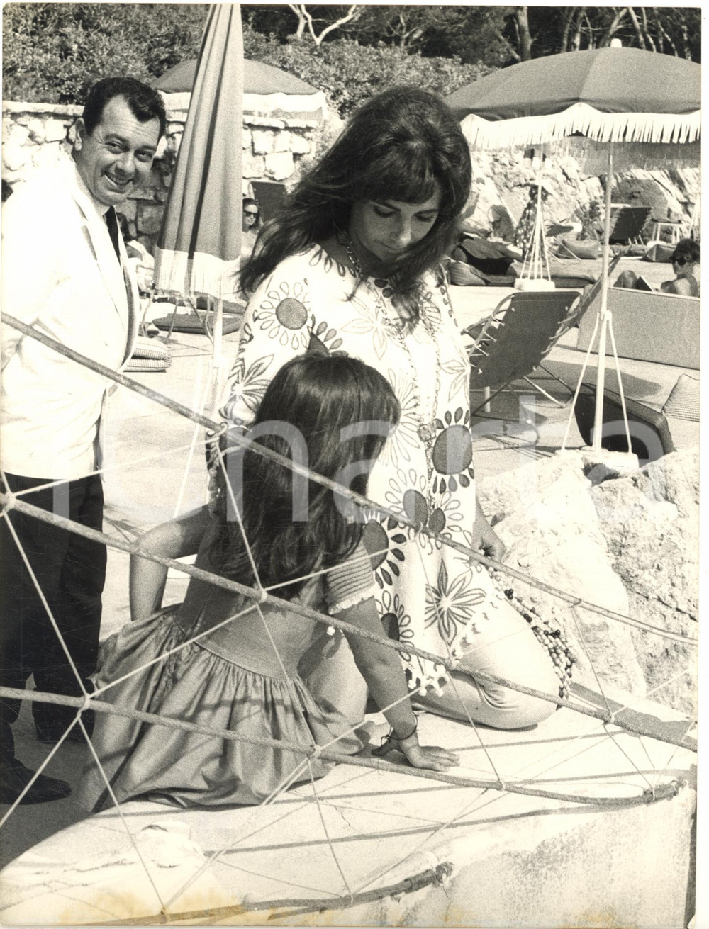 1965 FESTIVAL DI CANNES Liz TAYLOR in spiaggia con la famiglia - Foto 18x24 cm Fotografia d'epoca con didascalia coeva. CONDIZIONI: FAIR (piegature al lato destro; bruniture al margine inferiore) FORMATO: 18x24 cm    originale e autentica 1