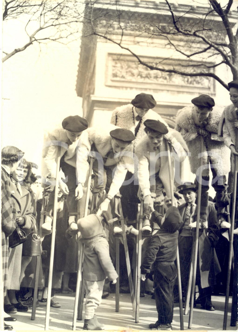 1955 PARIS Champs-Elysées - Jeunes landais sur des échasses saluent des enfants
