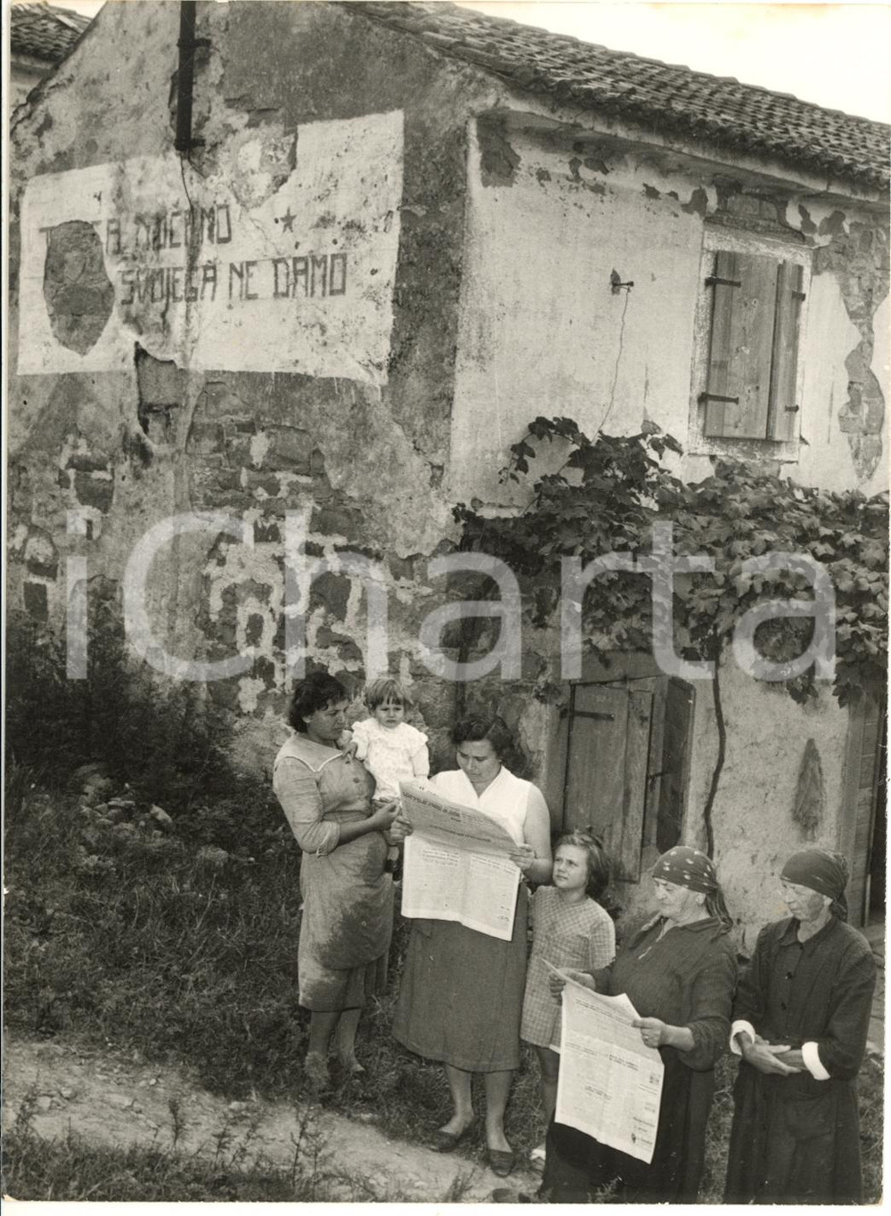 1954 SCOFFIE (SLOVENIA) Donne leggono la notizia del passaggio alla Jugoslavia Fotografia d'epoca, con didascalia dattiloscritta coeva, scattata a Scoffie (ex Albaro Vescov&agrave;, attuale Spodnje &Scaron;kofije).CONDIZIONI: FAIR (sovraimpressione circolare)FORMATO: 13x18 cm      originale e autentica 1
