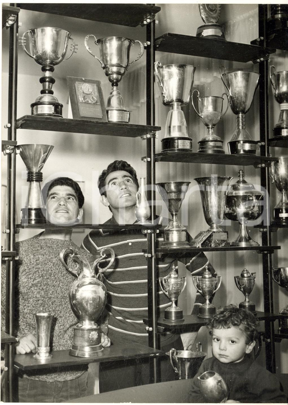 1958 BOLOGNA Tarquinio PROVINI mostra le sue coppe a Walter CHIARI *Foto 13x18  Fotografia d'epoca con didascalia coeva al verso.In primo piano si nota il figlio di Provini, Marzio.   CONDIZIONI: G FORMATO: 13x18 cm     originale e autentica 1