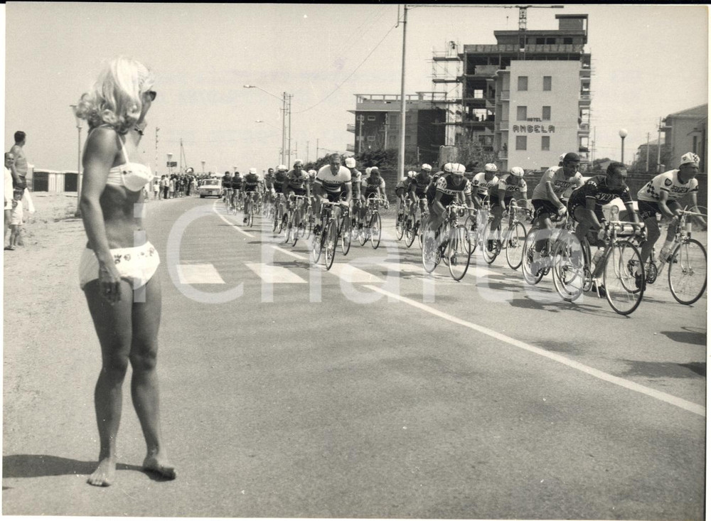 1967 GIRO D'ITALIA Riviera Adriatica - Ciclisti distratti da una bella bagnante Fotografia d'epoca con didascalia coeva al verso.Si vede sullo sfondo l'Hotel Angela. CONDIZIONI: G (ma lieve impressione del timbro)FORMATO: 18x13 cm     originale e autentica 1