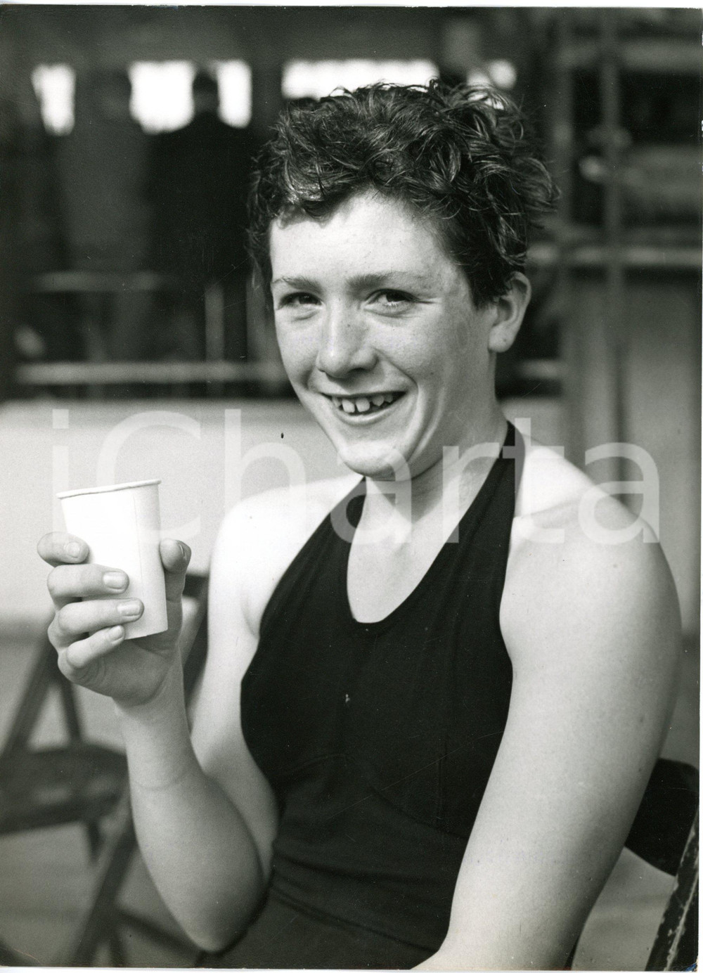 1960 BLACKPOOL Derby Baths - SWIMMING young champion Liz LONG enjoying drink  Fotografia d'epoca con didascalia dattiloscritta coeva.   CONDIZIONI: G (ma lieve abrasione al margine destro, piccola piegatura all'angolo inferiore sinistro) FORMATO: 15x21 cm     originale e autentica 1