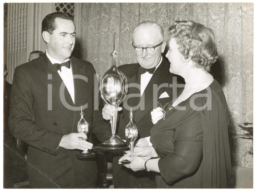 1960 LONDON Royal Automobile Club - Jack BRABHAM William LYONS Winifred HAWTHORN Fotografia d'epoca, con didascalia coeva al verso, stampata su carta sottile.La fotografia era stata scattata in occasione della consegna a Brabham dell'Hawthorn Memorial Trophy.CONDIZIONI: POOR (piegatura angolare all'angolo inferiore sinistro, graffi al lato sinistro, lieve sovraimpressione al centro)FORMATO: 20x15 cm    originale e autentica 1