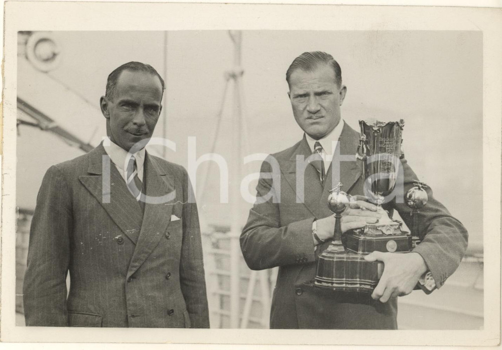 1934 NAPOLI - C.W.A. SCOTT Tom CAMPBELL BLACK winners LONDON-MELBOURNE Air Race  Rara fotografia, originale d'epoca, con didascalia dattiloscritta al verso.Sono ritratti i due piloti con la coppa vinta, allo sbarco a Napoli dal piroscafo Orford. FAIR/discreto difetti di stampa; minima piegatura angolare; margini lievemente rifilati Formato: 18x13 cm originale e autentica 1