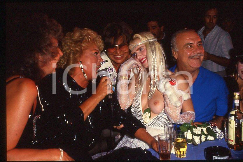 1980 ca CICCIOLINA Ilona STALLER - RAMBA - M. LEFAKIS - 35 mm vintage slide 19 Diapositiva d'epoca, in formato 35 mm.CONDIZIONI: GOODE' severamente vietata la riproduzione. Tutti i diritti sono riservati.Nella diapositiva ICharta mette in vendita, sul negozio eBay e in esclusiva sul sito "icharta" il proprio archivio composto da numerose diapositive e negativi fotografici d'epoca, tutti originali e autentici, che attraversano la storia del costume italiano tra gli la fine degli anni Sessanta e Novanta.Si tratta di uno sguardo inedito sull'attualità , la politica, la vita quotidiana, il gossip e la cultura, che fotografa il cambiamento della nazione in quest'ultimo scorcio del XX secolo. Un'occasione unica per il mercato del collezionismo, che vede finalmente disponibile un archivio eccezionale per vastità , tematiche e condizioni, in un settore (il negativo fotografico e la diapositiva) di assoluta novità e dalle interessanti prospettive di investimento.  GOOD/buono   originale e autentica 1