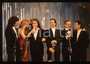 35mm vintage slide*1990 Festival SANREMO Johnny DORELLI POOH Gabriella CARLUCCI*   Diapositiva d'epoca, in formato 35 mm.Nella diapositiva i componenti del gruppo musicale POOH (Roby Facchinetti, Dodi Battaglia, Stefano D'Orazio e Red Canzian) con Gabriella Carlucci e Johnny Dorelli sul palcoscenico del Festival di Sanremo del 1990. CONDIZIONI: GOODE' severamente vietata la riproduzione. Tutti i diritti sono riservati. ICharta mette in vendita, sul negozio eBay e in esclusiva sul sito "icharta" il proprio archivio composto da numerose diapositive e negativi fotografici d'epoca, tutti originali e autentici, che attraversano la storia del costume italiano tra gli la fine degli anni Sessanta e Novanta.Si tratta di uno sguardo inedito sull'attualit&agrave;, la politica, la vita quotidiana, il gossip e la cultura, che fotografa il cambiamento della nazione in quest'ultimo scorcio del XX secolo. Un'occasione unica per il mercato del collezionismo, che vede finalmente disponibile un archivio eccezionale per vastit&agrave;, tematiche e condizioni, in un settore (il negativo fotografico e la diapositiva) di assoluta novit&agrave; e dalle interessanti prospettive di investimento.  originale e autentica 1