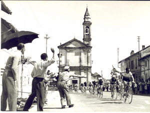 1957 CICLISMO GIRO D'ITALIA MAGENTA Passaggio della prima tappa *Foto 18x13 cm  Fotografia d'epoca con didascalia coeva al verso.  CONDIZIONI: fair (lievi piegature angolari; sovraimpressione al margine inferiore) FORMATO: 18x13 cm     originale e autentica 1
