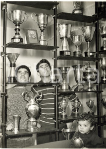 1958 BOLOGNA Tarquinio PROVINI mostra le sue coppe a Walter CHIARI *Foto 13x18  Fotografia d'epoca con didascalia coeva al verso.In primo piano si nota il figlio di Provini, Marzio.   CONDIZIONI: G FORMATO: 13x18 cm     originale e autentica 1