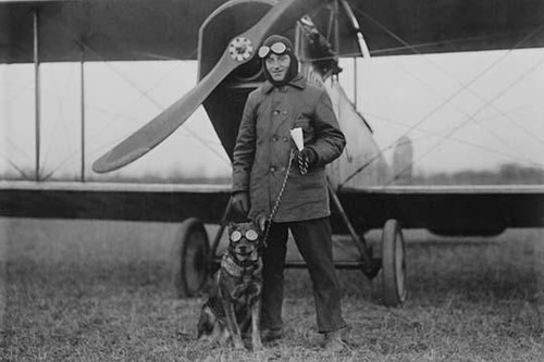 Aviator and His dog wear goggles in front of his Biplane