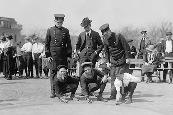 Three Young Boys Crouch in front of three men - the boys hold their marbles