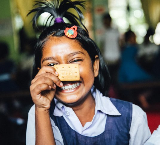 Smiling child holding a biscuit from a school feeding program