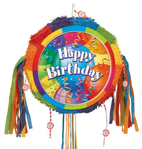 A round, rainbow-colored piñata featuring a bold "Happy Birthday" text in the center, surrounded by balloons, streamers, and confetti. The edges are decorated with fringed tissue paper in bright colors, and long, multicolored ribbons hang from the sides and bottom for a pull-string candy release.