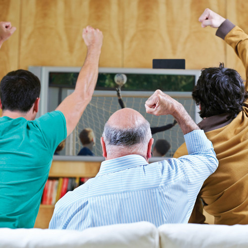 Three guys on a couch cheering while watching sports on a television in front of them