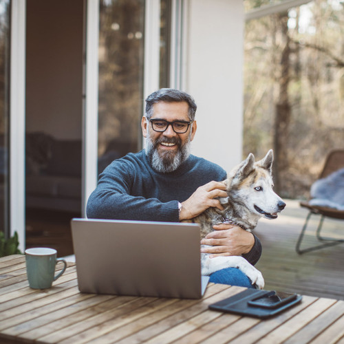 Man using wifi from the Extreme 2.0 High-Performance Outdoor WiFi Extender on a laptop outside of a home with his dog in his lap