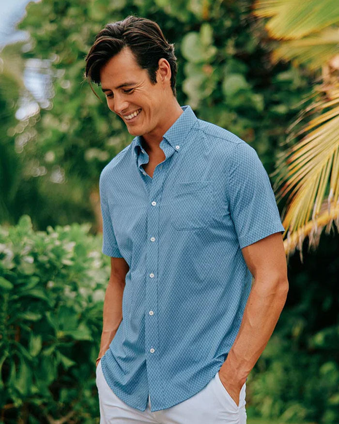 a man wearing short sleeve blue shirt standing with both hands in pockets 