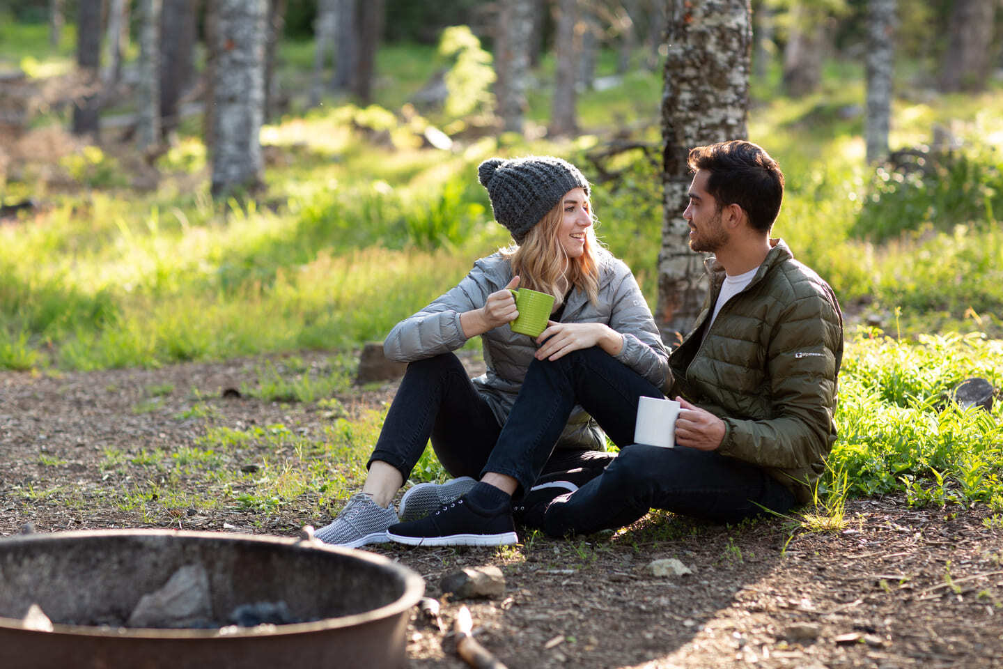 man and women wearing winter outerwear drinking tea in the woods