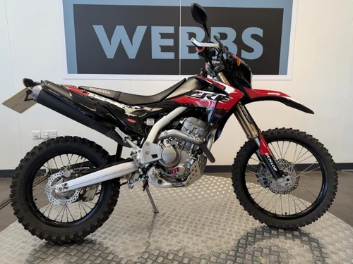 Honda CRF 250 LA-K motorcycle at Webbs Motorcycles. The off-road dirt bike features a black, red, and white color scheme, knobby tires, and a sleek design suitable for motocross riding.