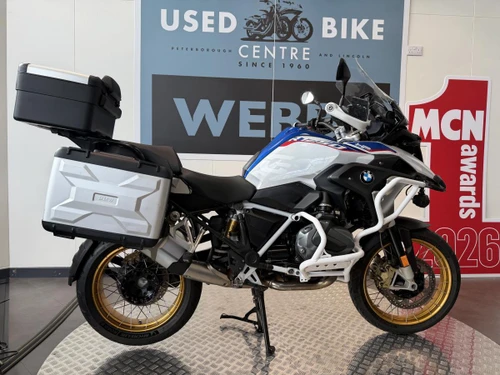 BMW R 1250 GS RALLYE TE motorcycle at Webbs Motorcycles dealership, featuring a white body with blue and red accents, gold wheels, and side panniers for touring and adventure riding.