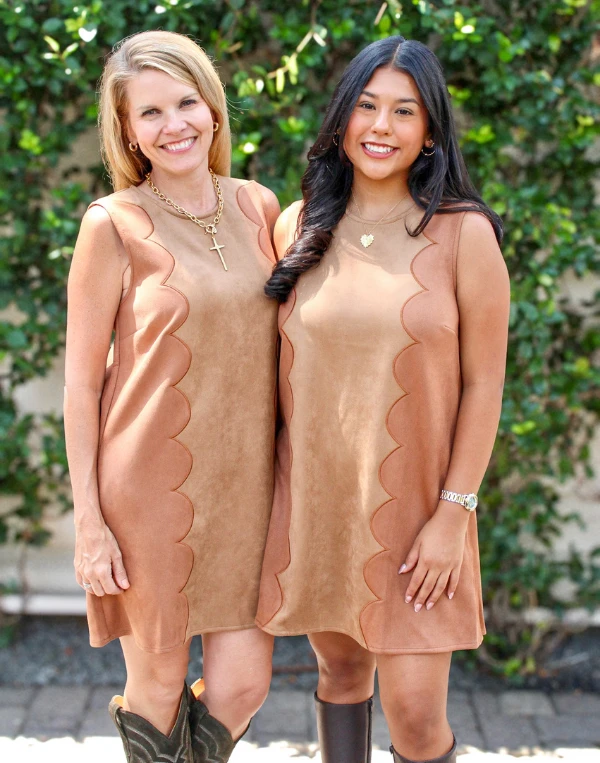 Mother and daughter wearing matching camel scalloped-trim shift dresses with brown boots, standing outdoors at Magpies Gifts Mod Suede Block Dress.