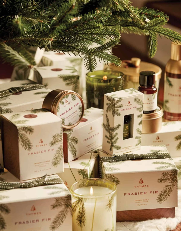 Thymes Frasier Fir holiday collection featuring beautifully packaged candles, home fragrance products, and gift sets with festive evergreen designs, surrounded by fresh pine branches and warm candlelight.