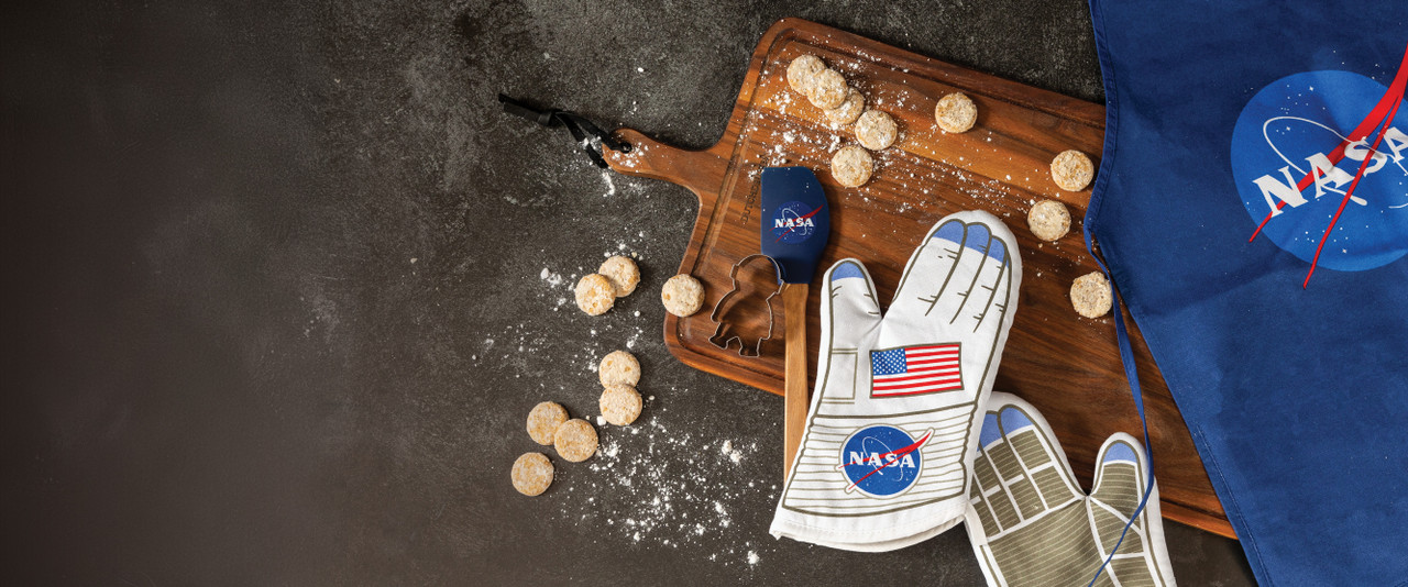 NASA themed apron, spatula, oven mitts, and cookie cutter with cookies scattered on cutting board