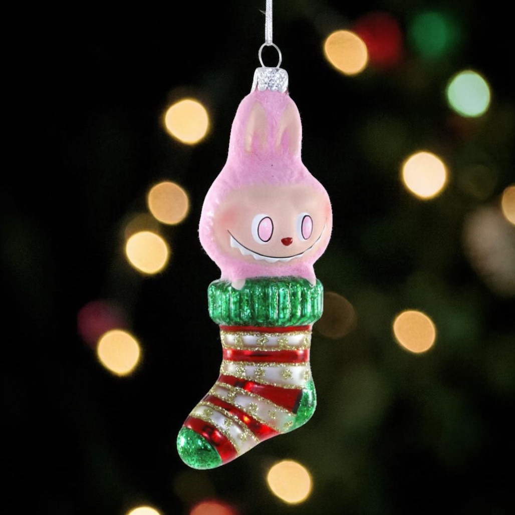 Glass ornament with pink fuzzy monster sitting in a striped Christmas stocking.
Fuzzy Monster Stocking ornament with red, white, and green glittered stocking details.
Hanging glass monster stocking ornament measuring 1.5 x 1.25 x 4.75 inches.