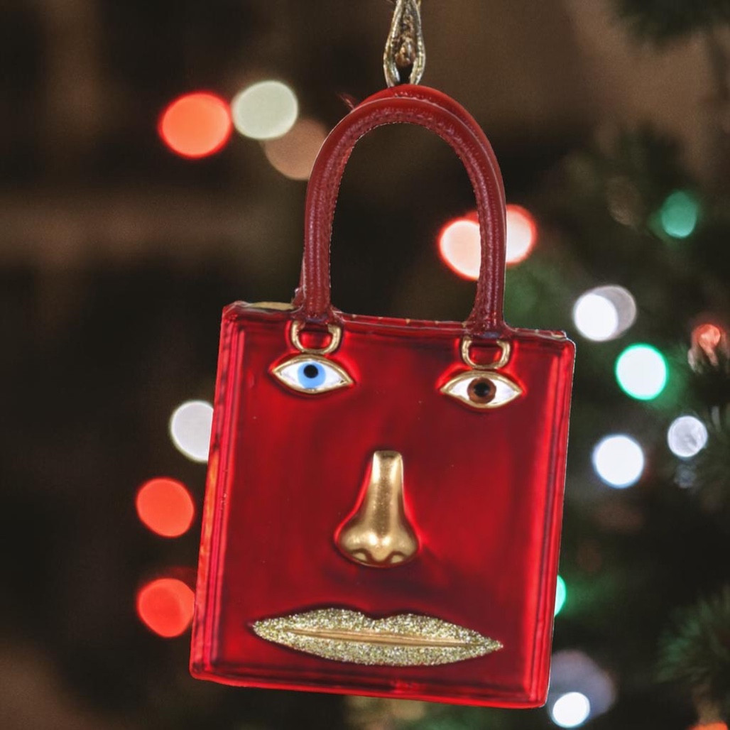 Red glass handbag ornament with face design, gold nose, and glitter lips.
Fashion-themed purse ornament with two handles and mismatched eye details.
4.25 inch Le Visage Bag glass ornament