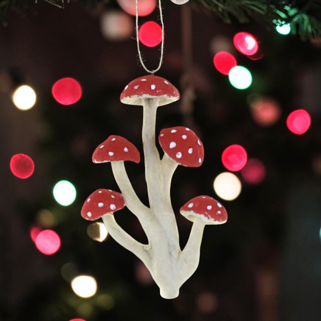 Paper mache mushroom cluster ornament with red caps and white spots.
Woodland Christmas ornament with white stems and five red mushroom tops.
Cotton mushroom cluster ornament hanging from a gold cord.