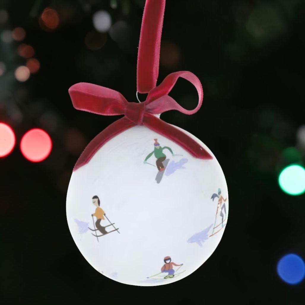 White glass bauble ornament with illustrated downhill skiers.
Ski-themed Christmas ornament with red ribbon bow and hanging loop.
Round glass skier ornament for winter sport holiday decorating.