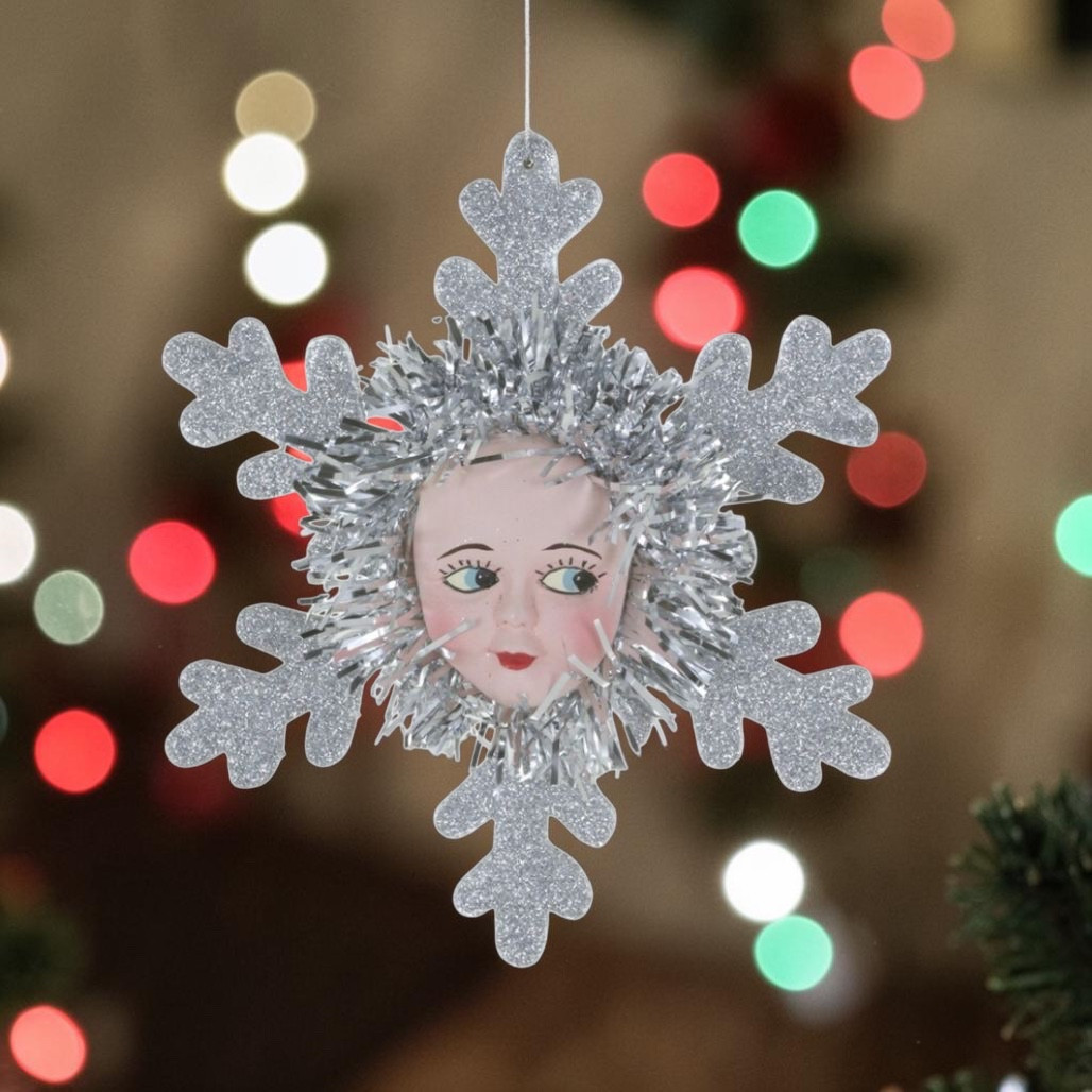 Paper mache doll face snowflake ornament with silver glitter snowflake points and shiny tinsel trim.
Vintage-inspired Christmas ornament with painted doll face centered in a silver snowflake.
Doll Face Snowflake ornament measuring 5.5 x 1.5 x 6 inches.